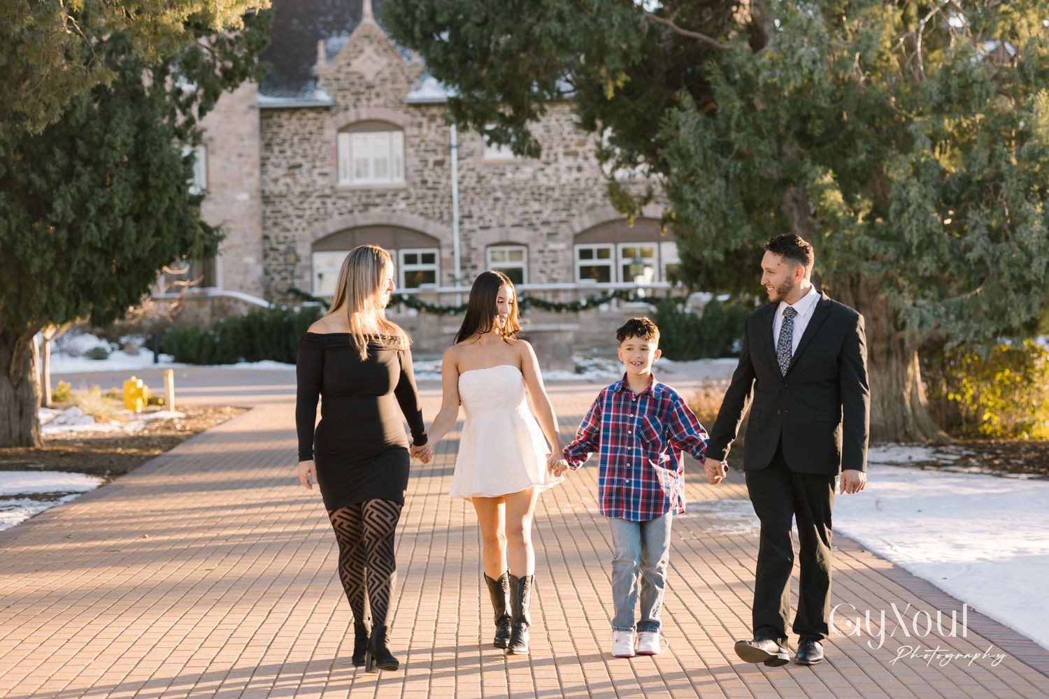Family walking together on brick pathway with stone building in background.