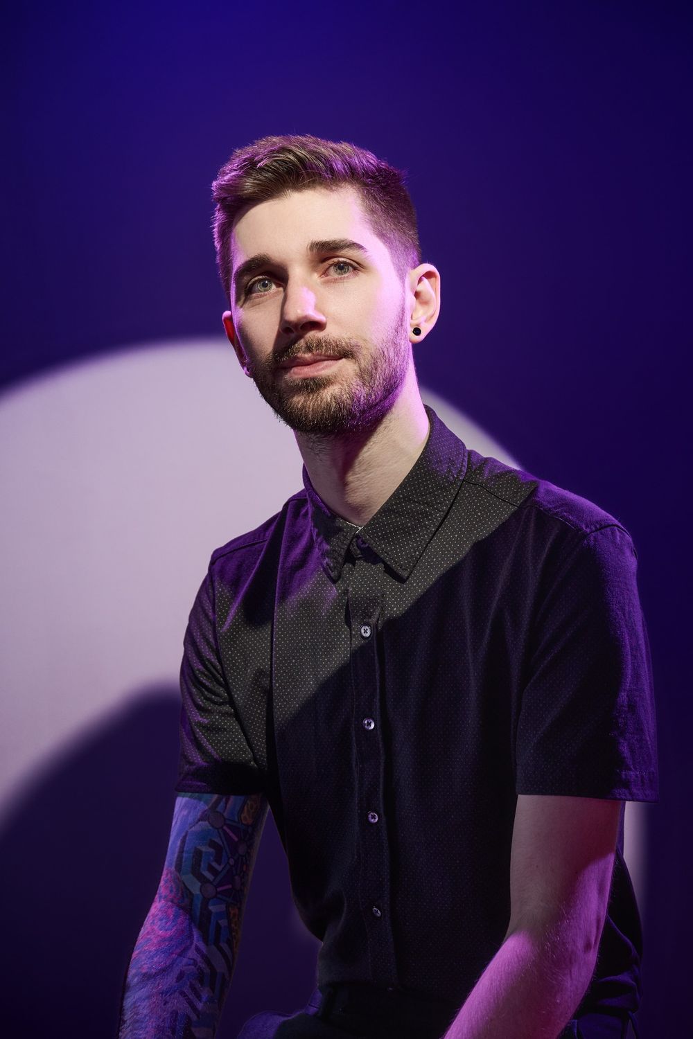 Singer performing on stage wearing a black shirt under dramatic purple lighting during a concert performance.