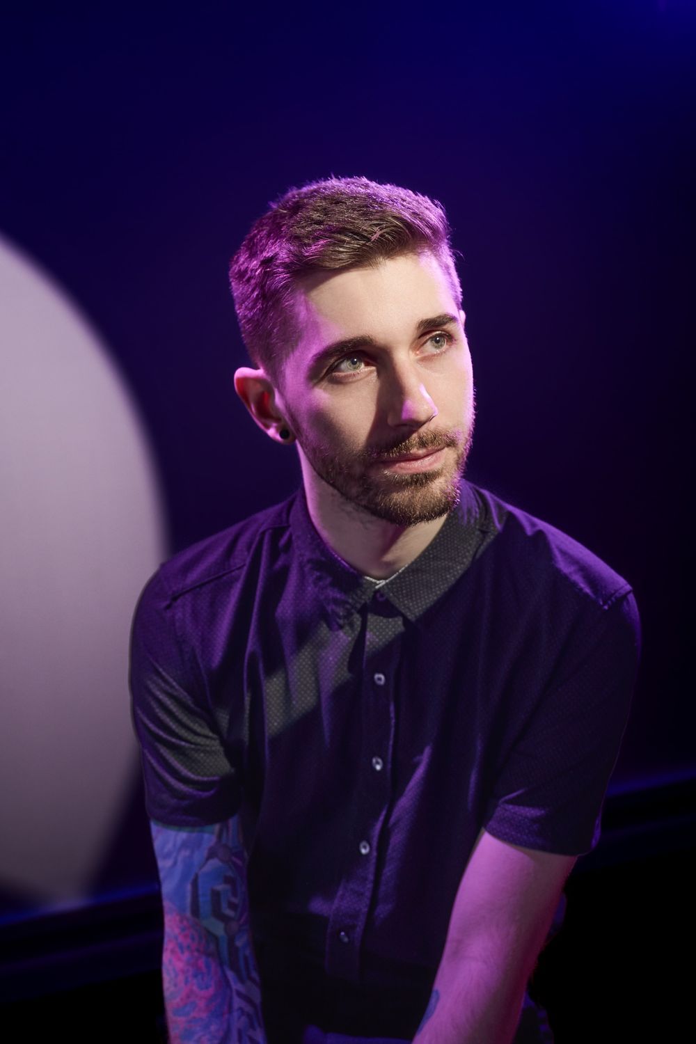 Artist performs on darkened stage illuminated by purple lighting while wearing a black shirt.