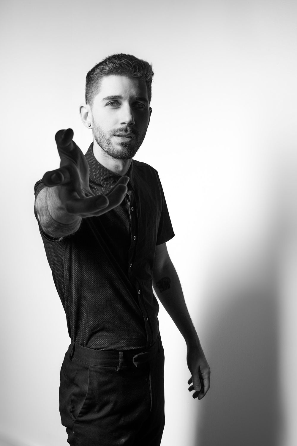 Artistic black and white portrait of a person in dark clothing reaching forward against a light background.
