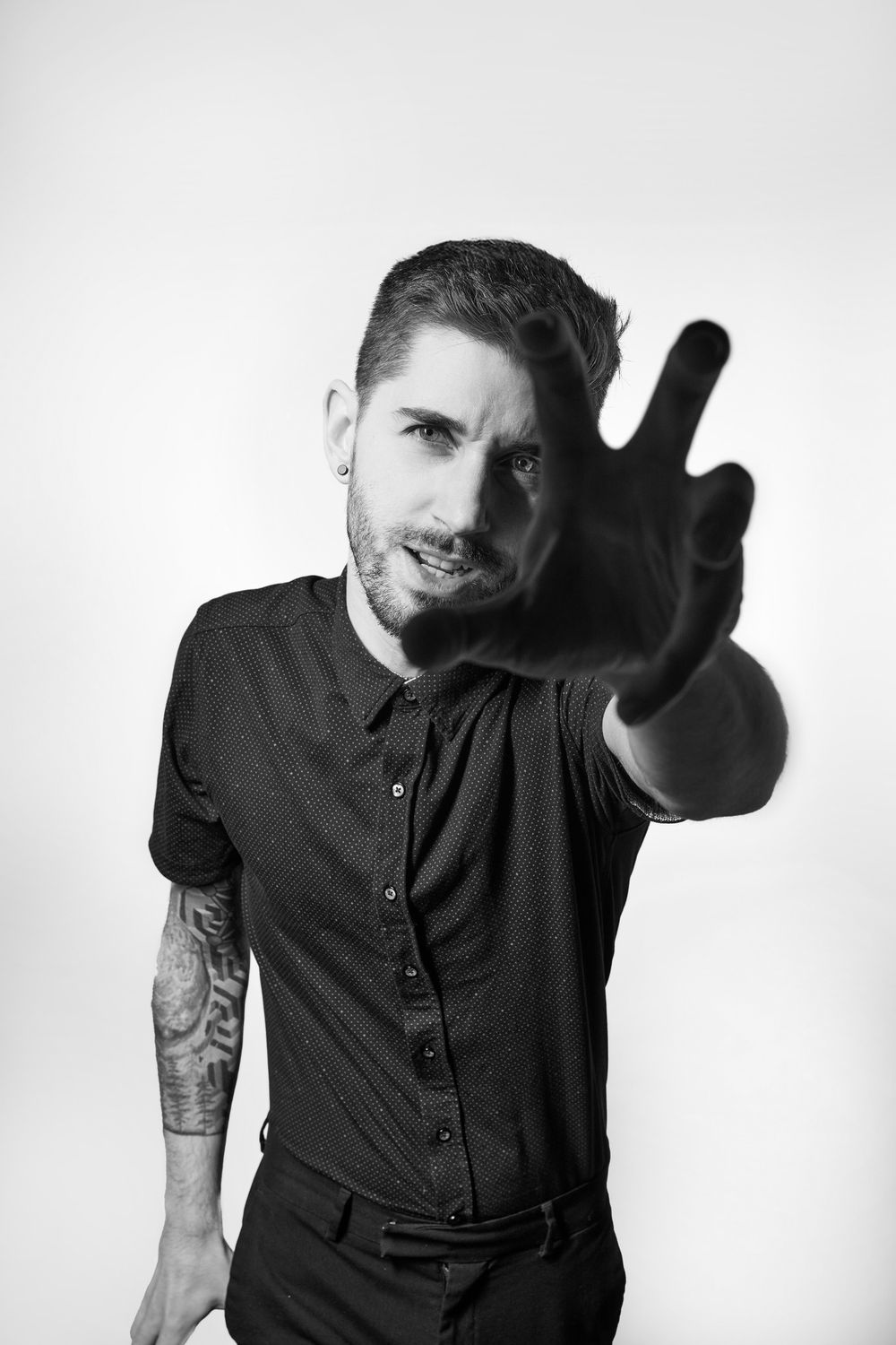 Black and white portrait of someone in dark clothing making a peace sign gesture toward the camera.