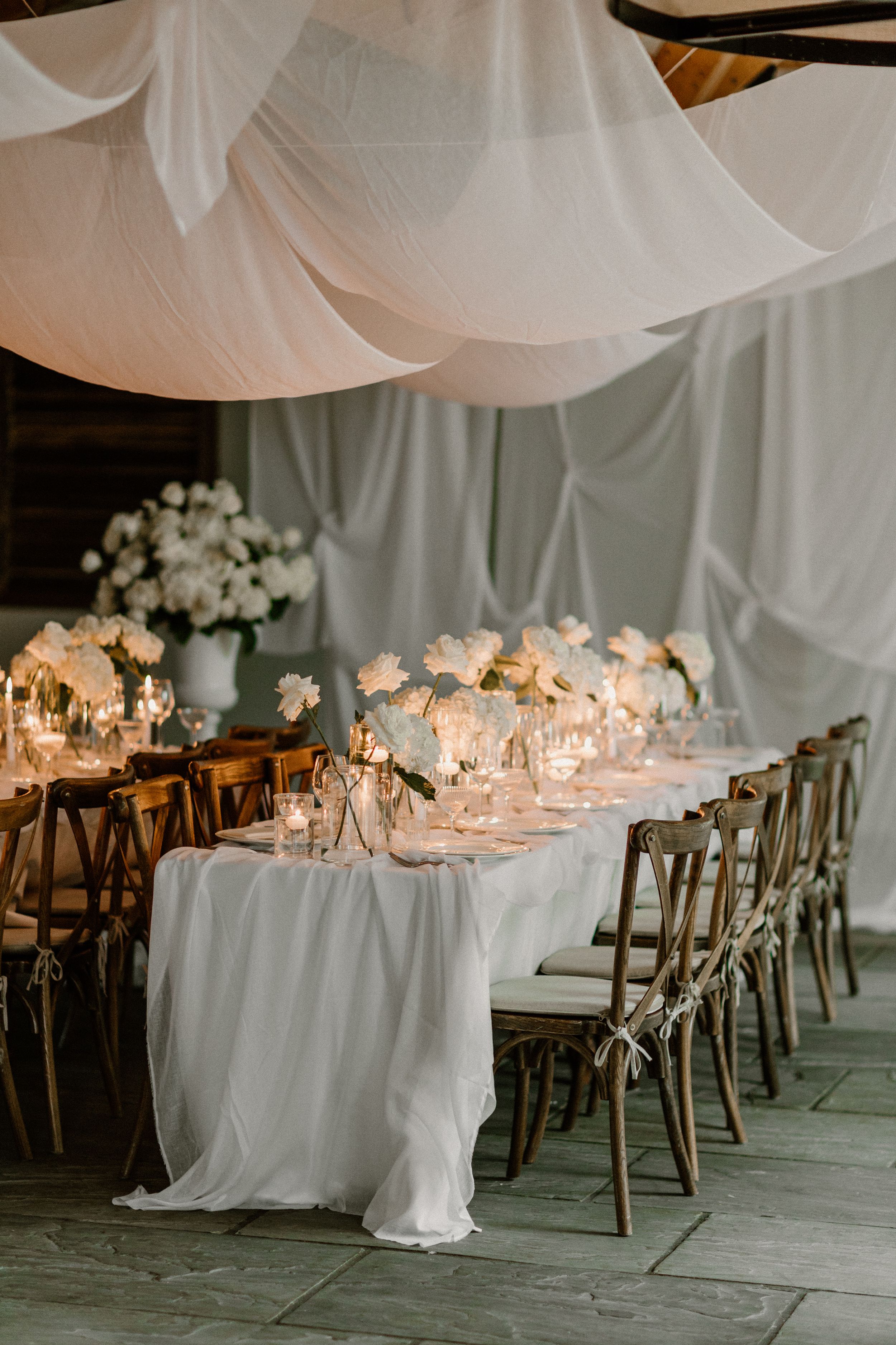 Romantic wedding reception table setting with white draping and floral centerpieces.