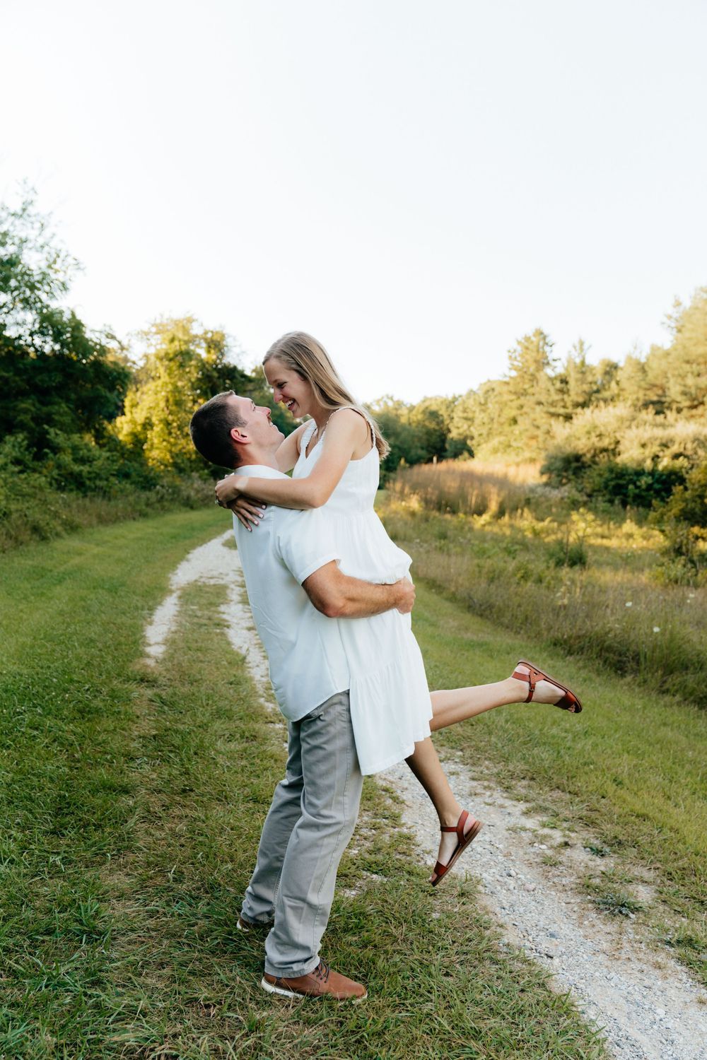 Joyful couple shares a romantic lift moment on a country path during sunset.