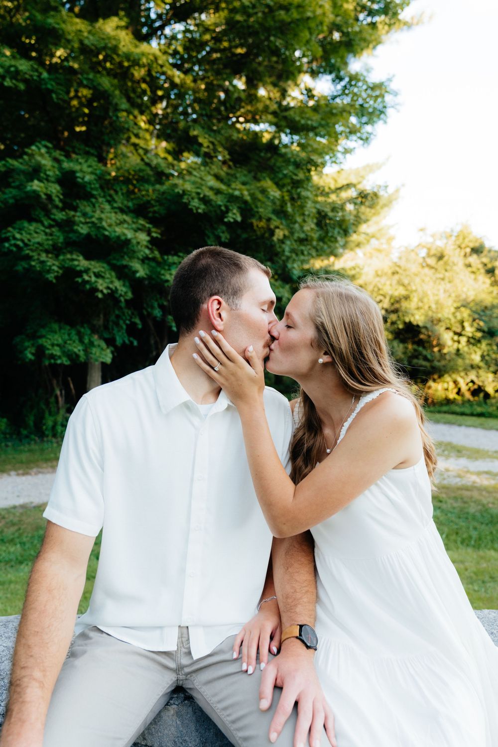 Couple in white outfits shares an intimate kiss outdoors during a summer photoshoot.