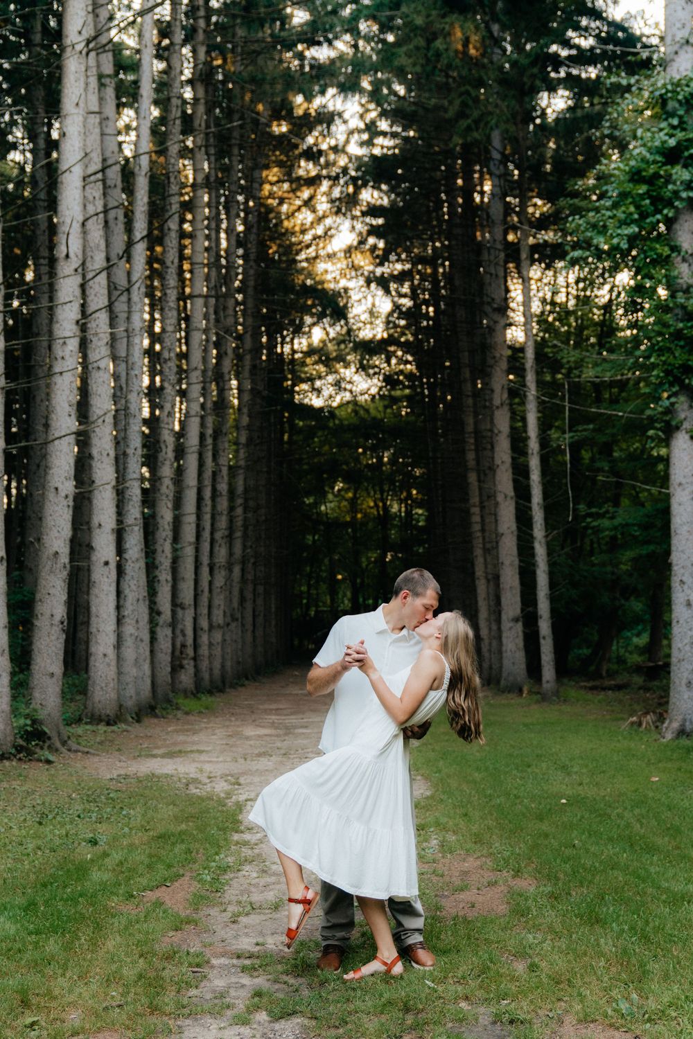 Romantic dance pose between tall pine trees on forest path at sunset.