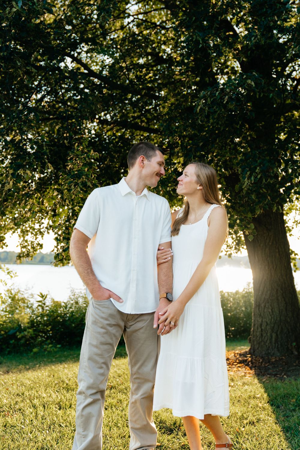 Couple in coordinated white outfits shares loving glance in golden summer light.