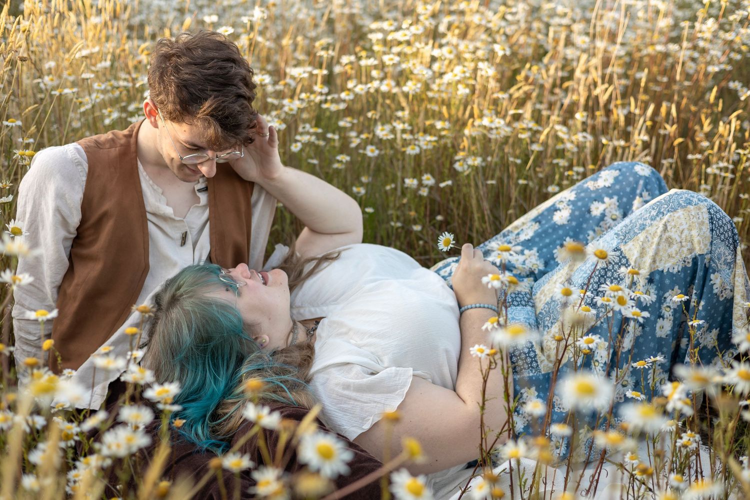 Couple portrait laying together in a field of daisies during golden hour.