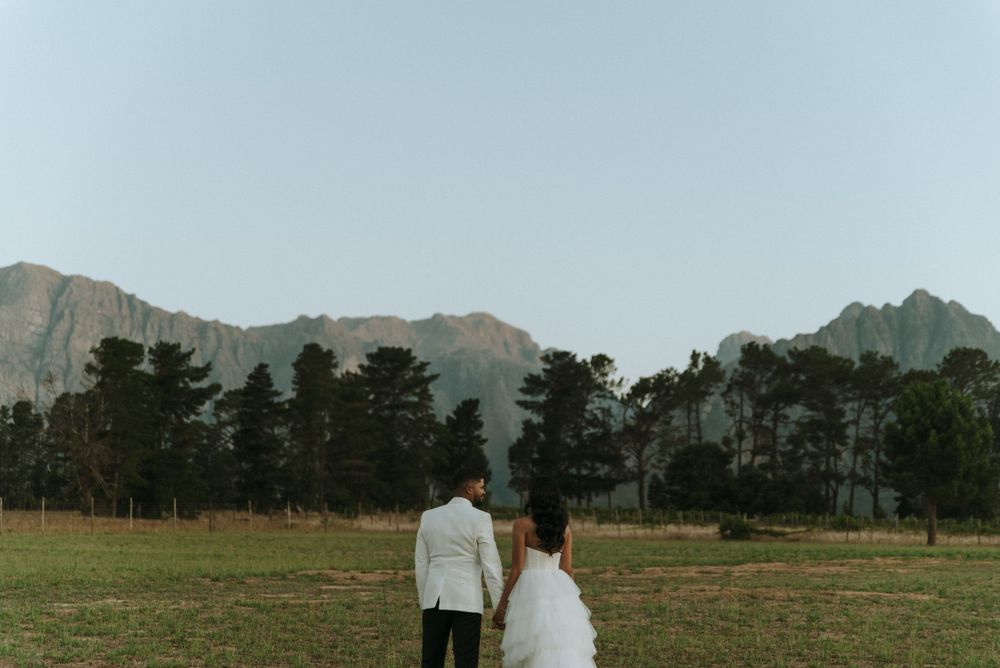 Wedding couple stands before mountain landscape in outdoor setting.