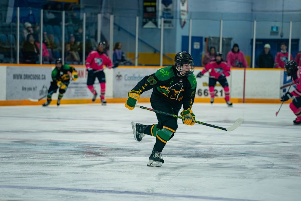 Hockey player in green uniform skates across ice during competitive game.
