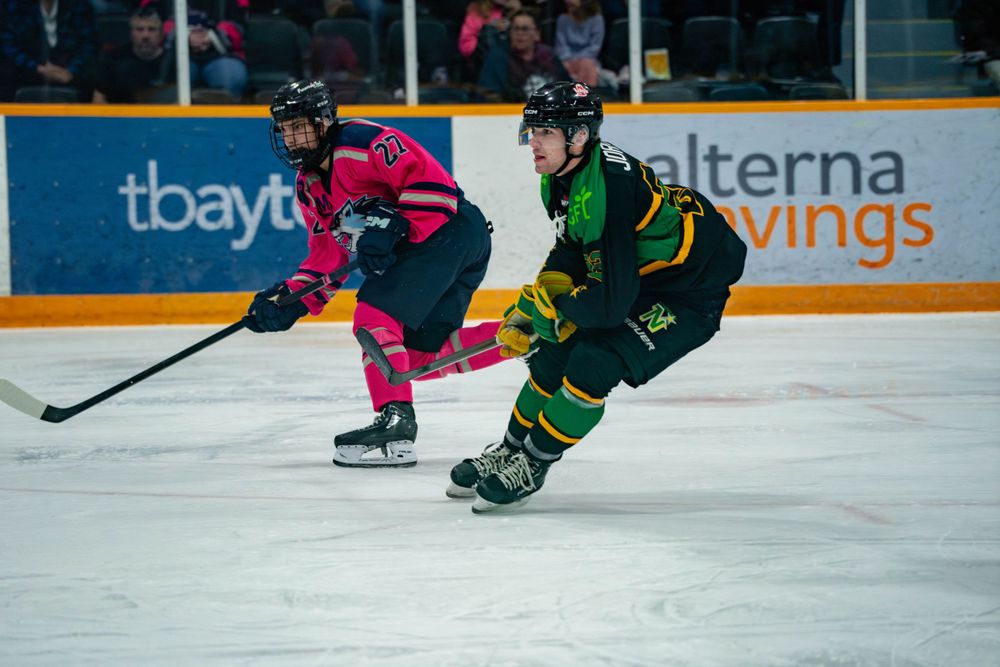 Two hockey players from opposing teams compete for the puck during an ice hockey match.