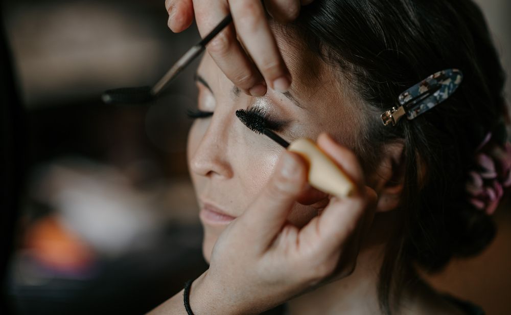 Close-up of makeup artist applying mascara to a bride with decorative hair clip.