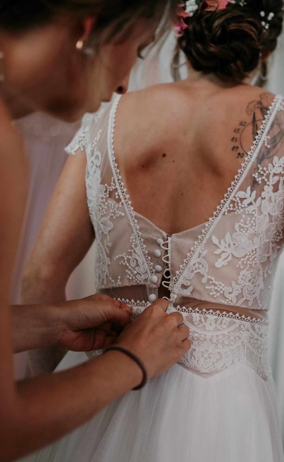 Close-up of intricate lace back wedding dress being buttoned by a bridesmaid.
