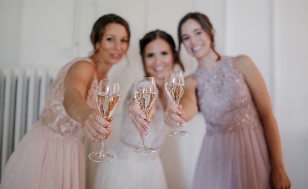 Bride and two bridesmaids smiling while toasting with champagne flutes.