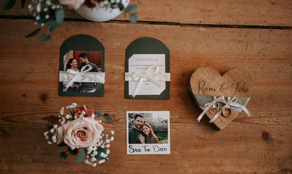 Wedding stationery flat lay featuring save the date cards, floral decorations, and a heart-shaped ring box.