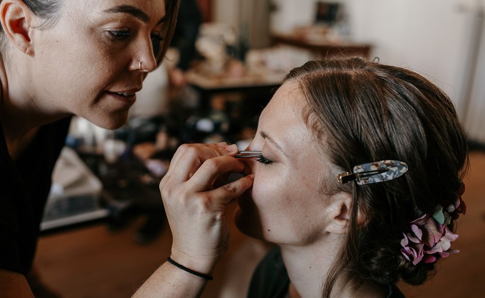 Makeup artist carefully applying eyeliner to a bride with floral hair accessory.