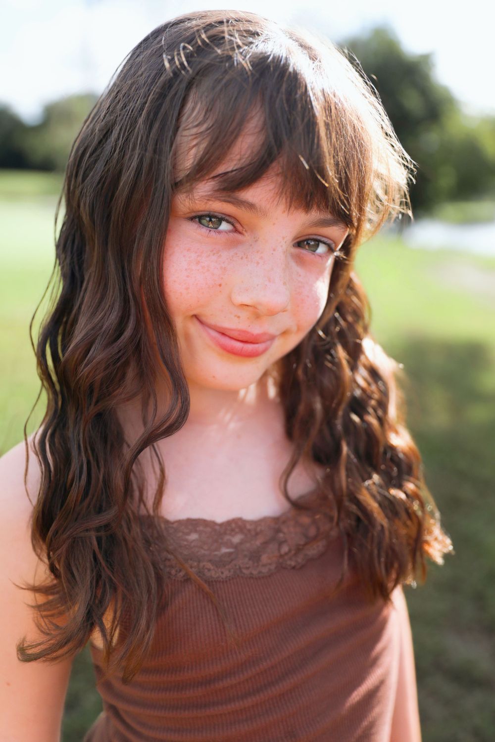 Close-up portrait with soft lighting showing hair with bangs and warm smile.