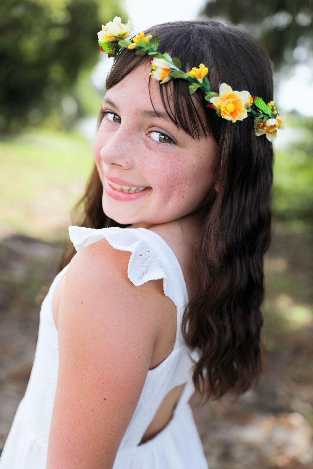 Outdoor portraits with flower crown and white sleeveless dress against trees.