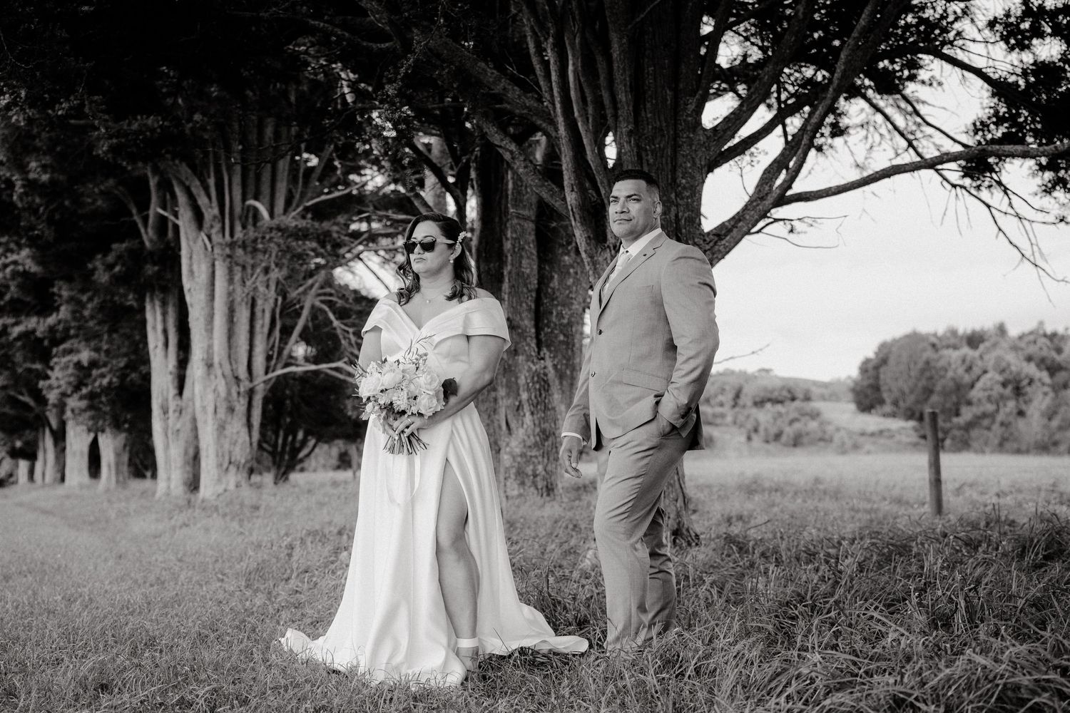 Black and white portrait of couple standing among tall trees during wedding photoshoot.