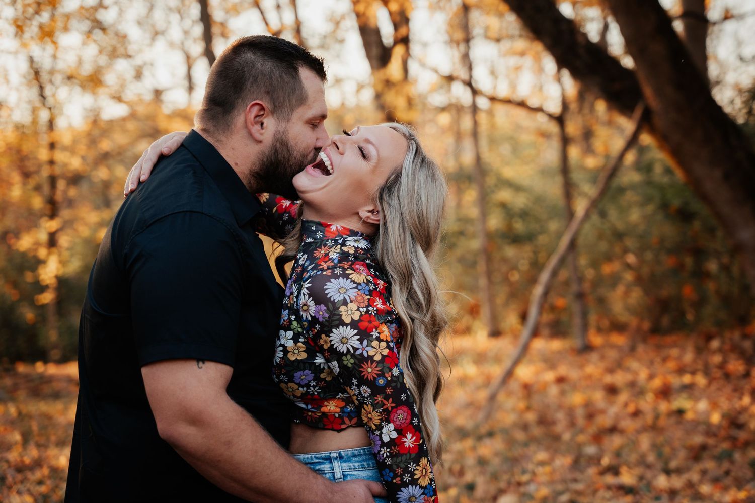 A couple shares a joyful moment together in an autumn forest setting.