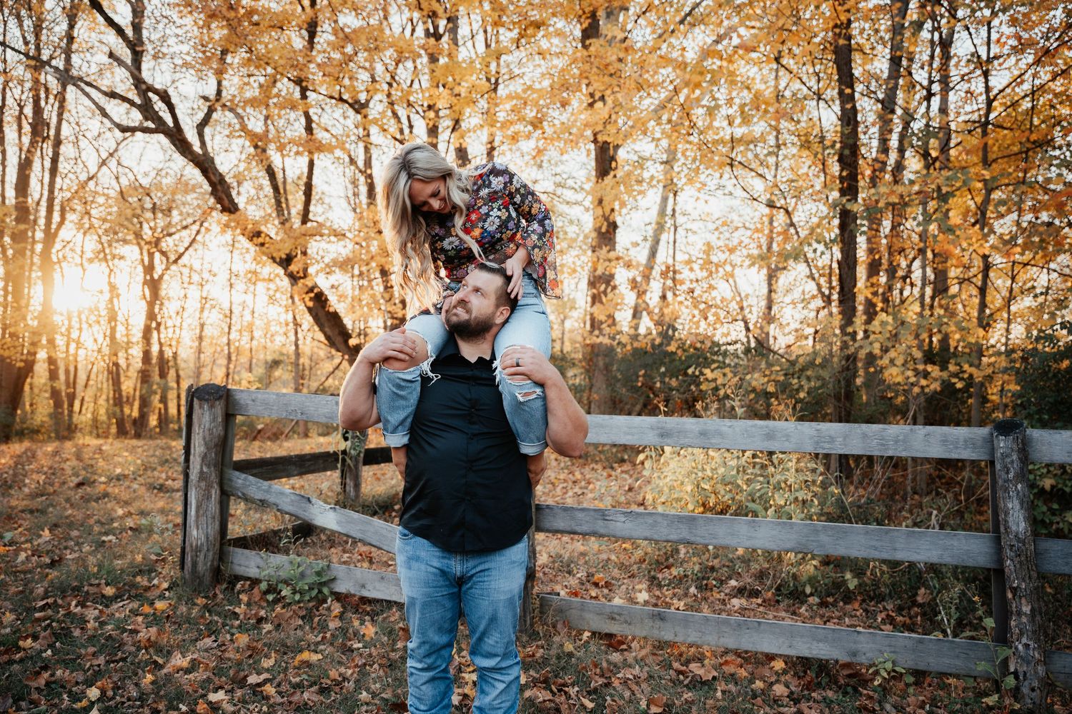 A playful shoulder ride moment captured in front of an autumn forest fence.