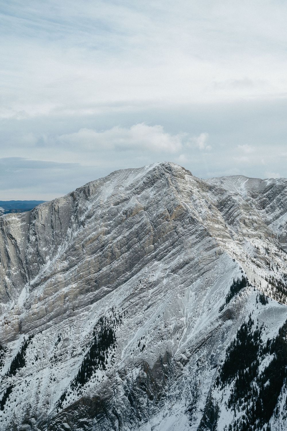Dramatic snow-covered mountain peak rising against bright winter sky.