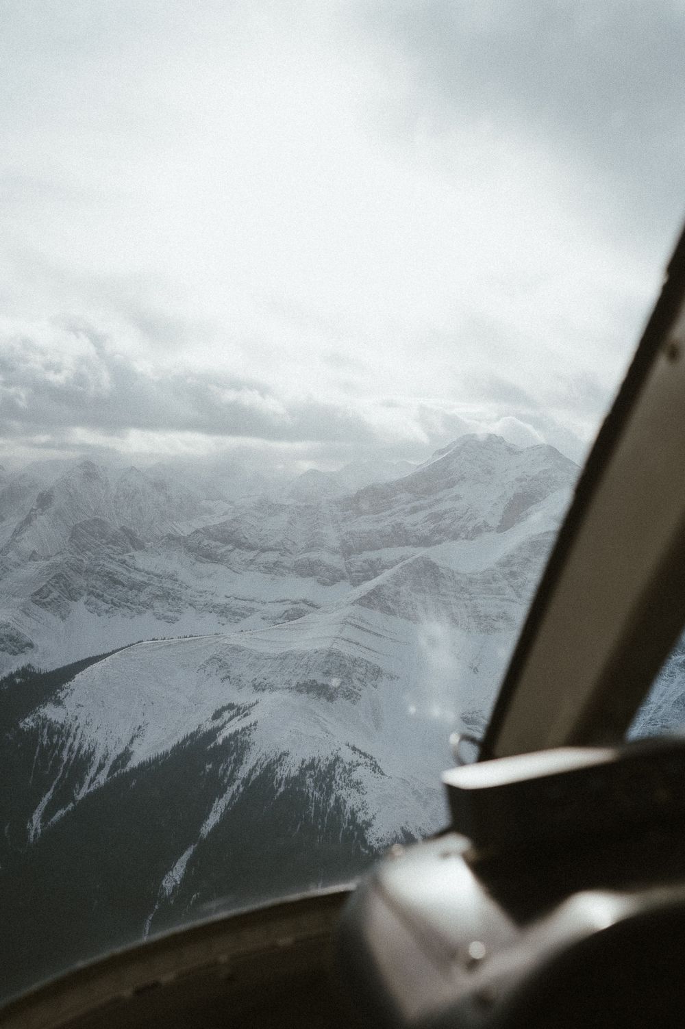 Snow-covered mountain peaks viewed through helicopter window with control panel visible.
