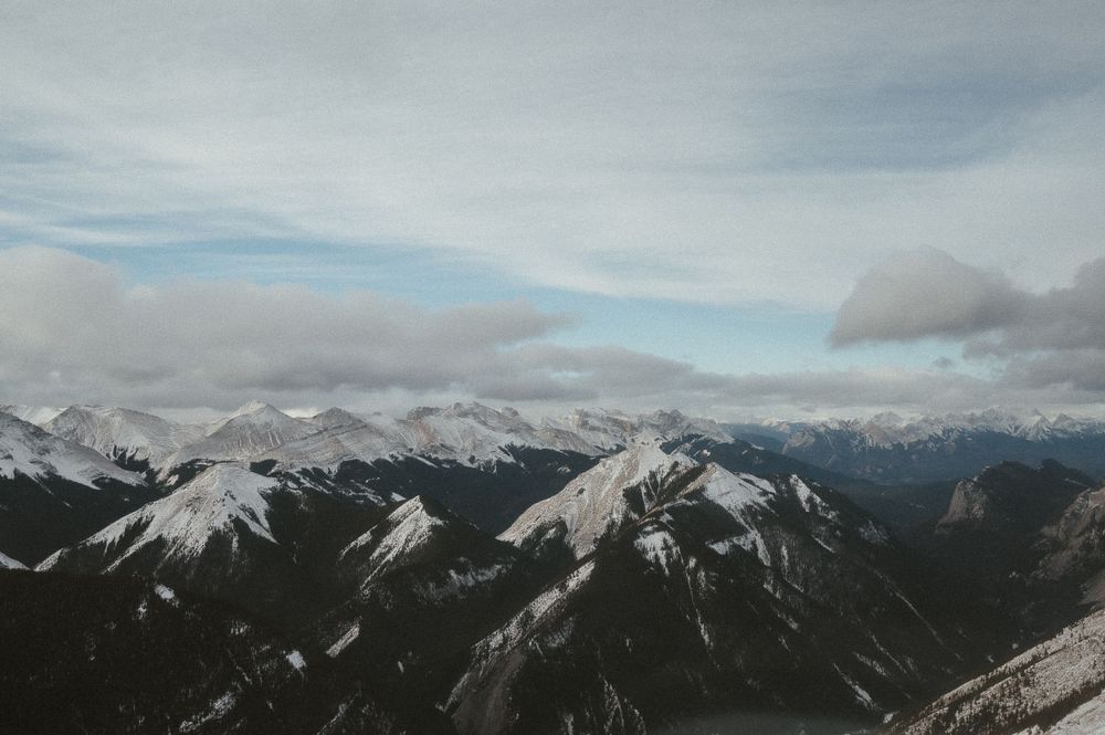 Snow-capped mountain peaks stretch across a dramatic mountain range under cloudy skies.