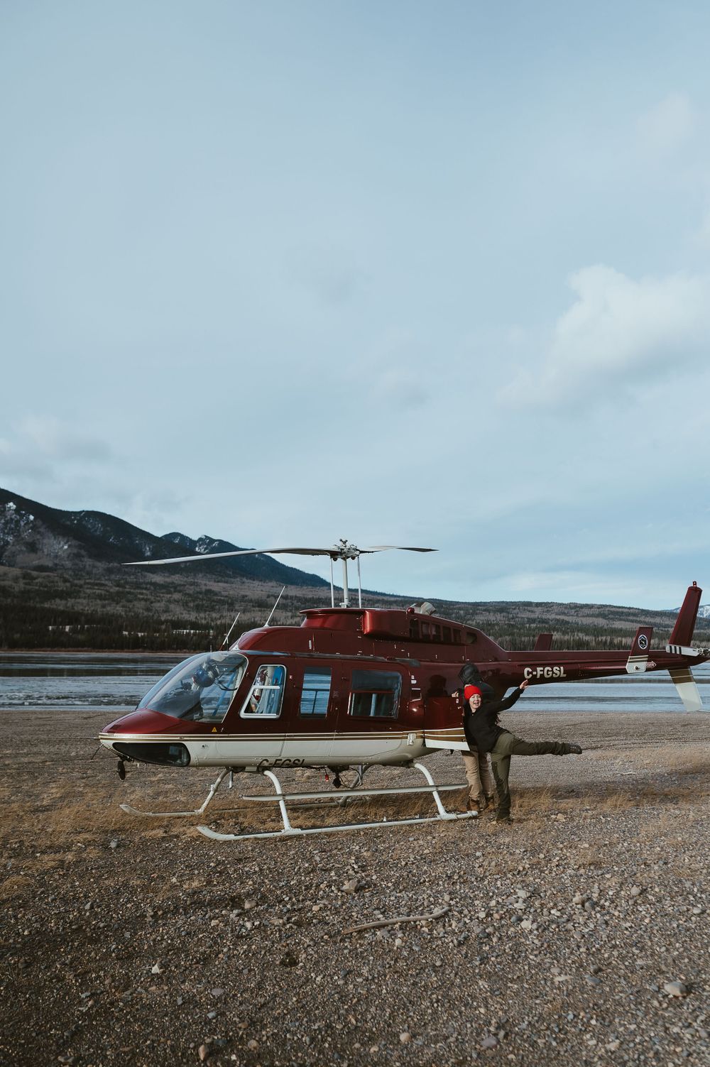Red Bell helicopter parked on gravel with mountains in background.