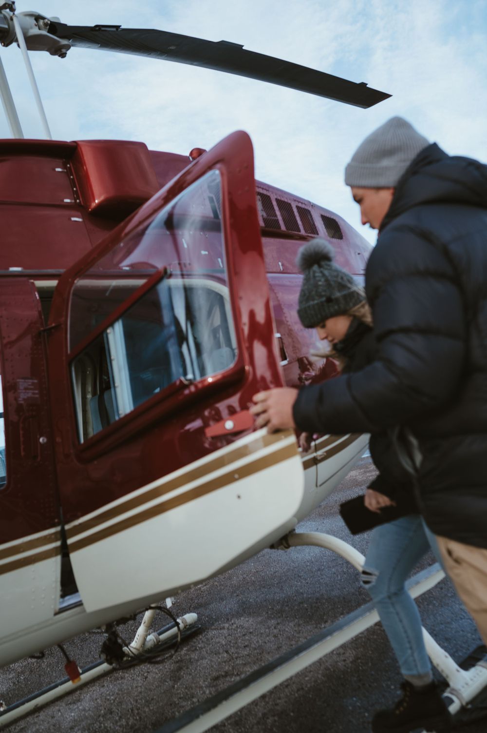 Passengers boarding a red and white helicopter during a winter day.