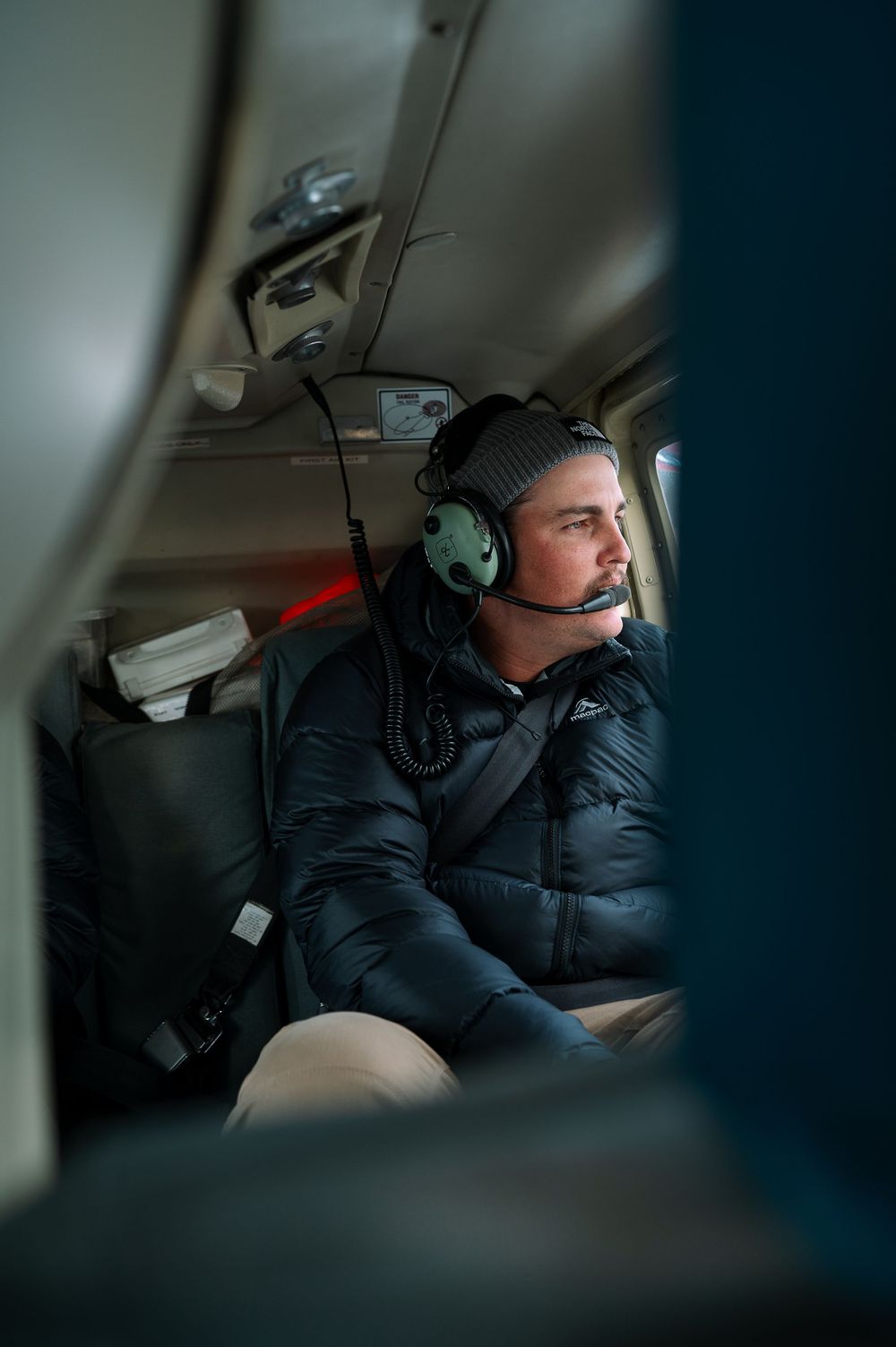 An occupant in winter gear and headset inside the helicopter cockpit.