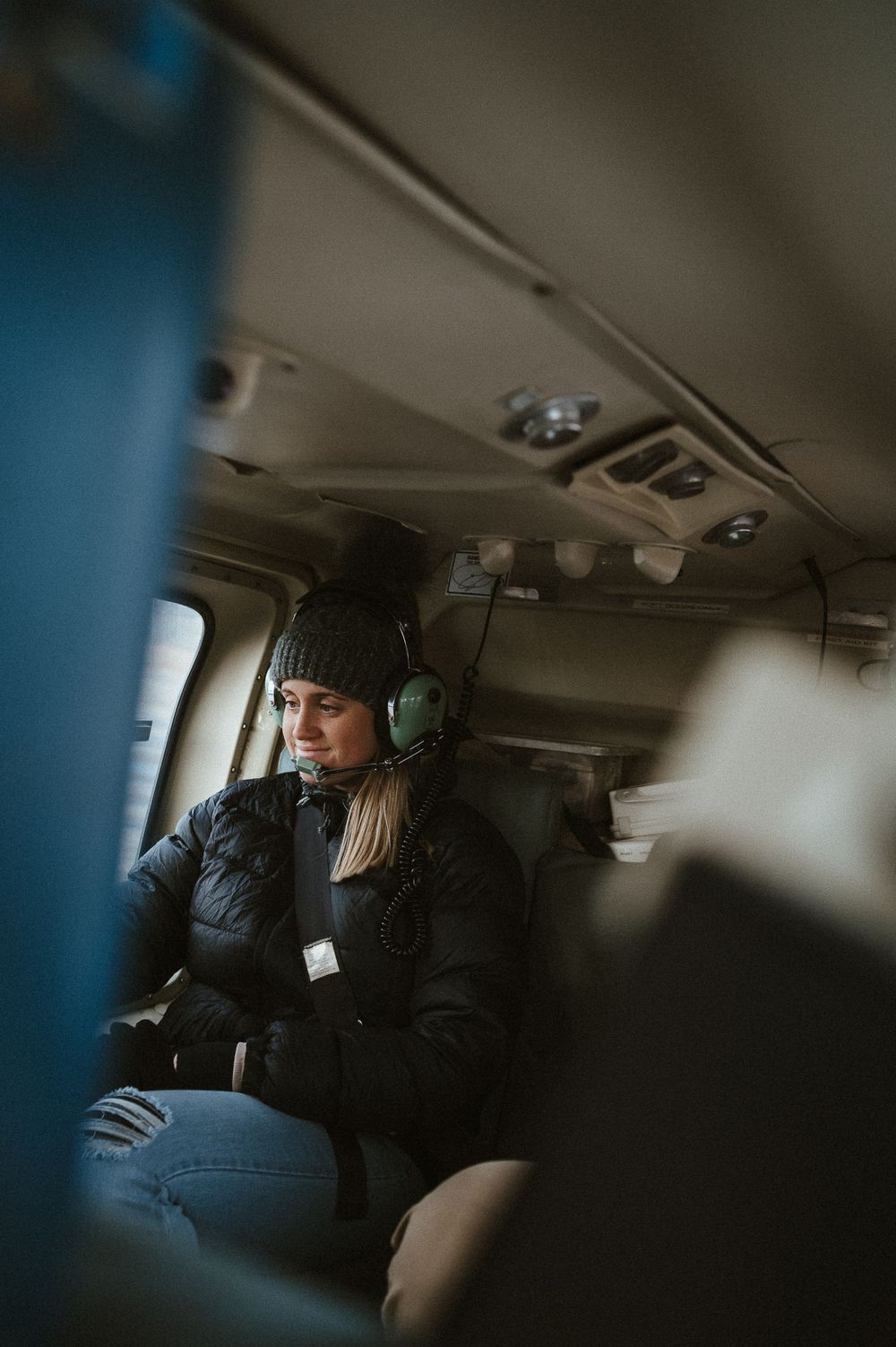 A passenger wearing a winter coat and headset sits inside the helicopter cabin.