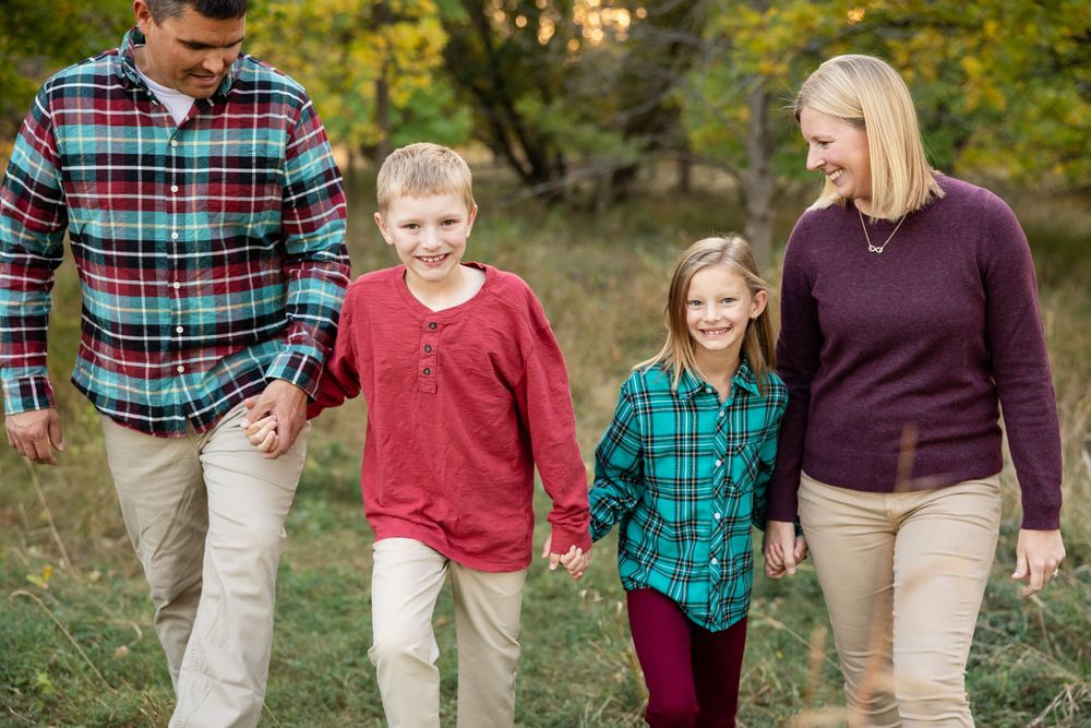 A family walks hand in hand through an autumn landscape wearing coordinated plaid and casual attire.
