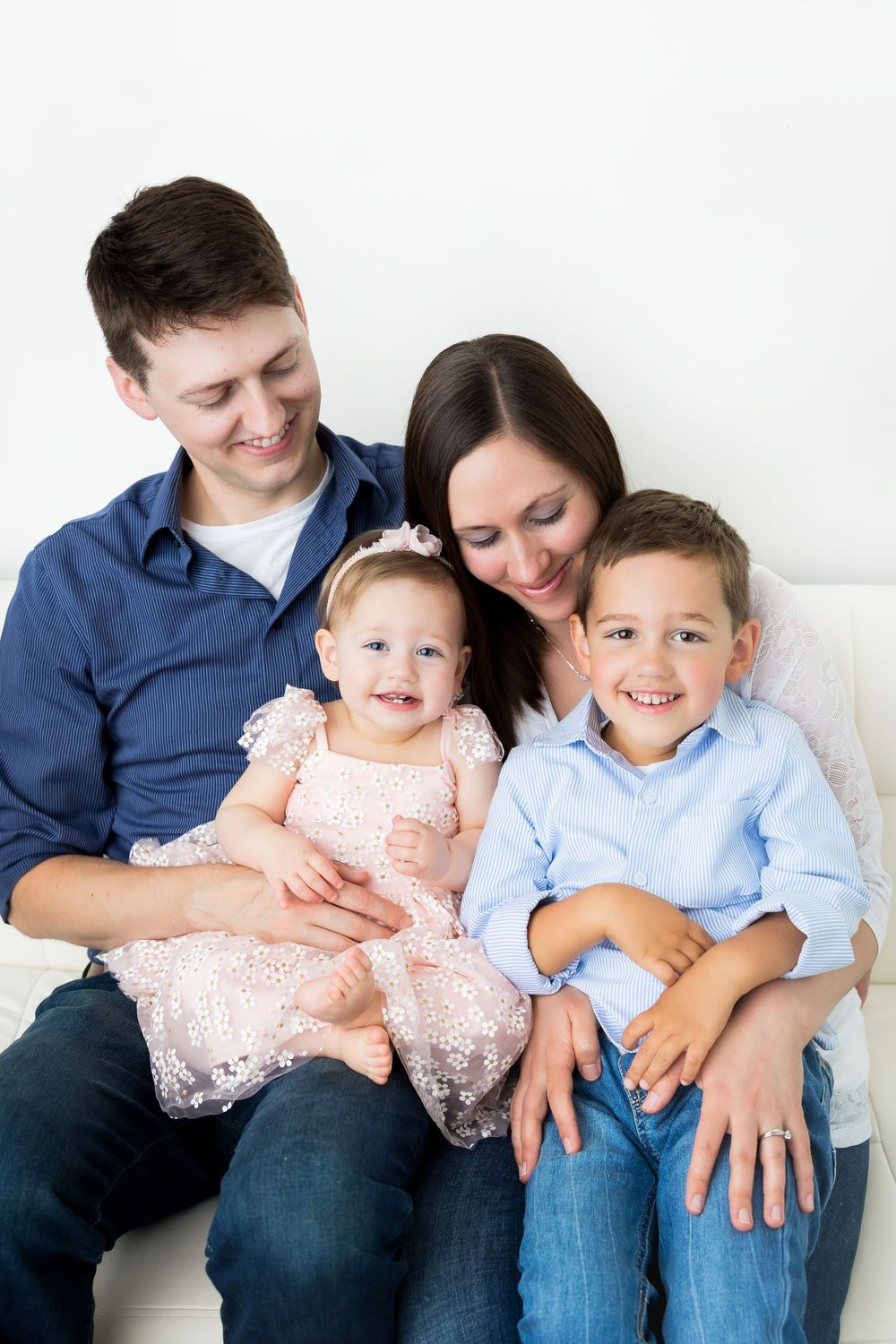 A happy family of four sits together smiling and laughing against a white background.