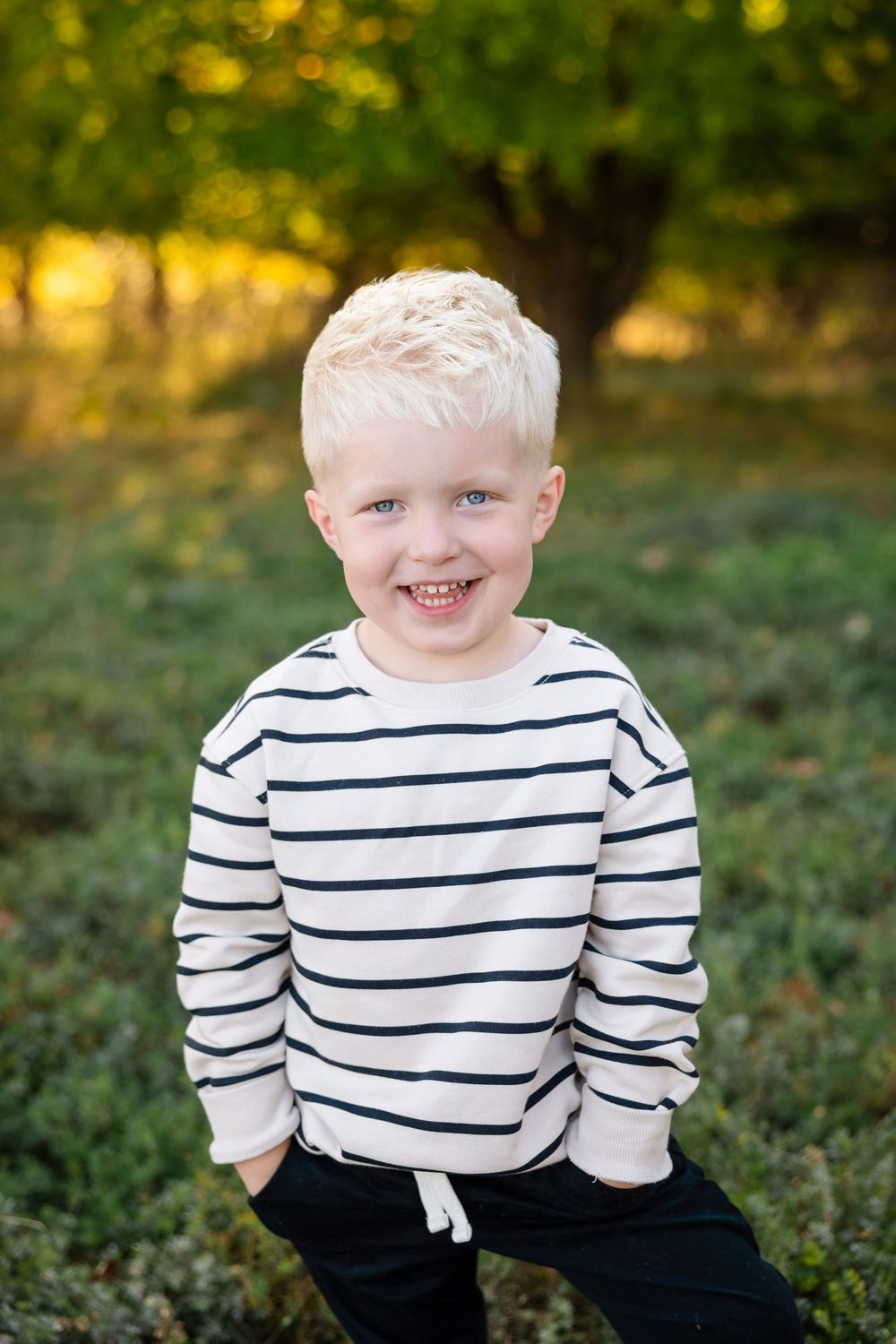 Toddler wearing a white and navy striped sweater smiling while playing outdoors in autumn setting.
