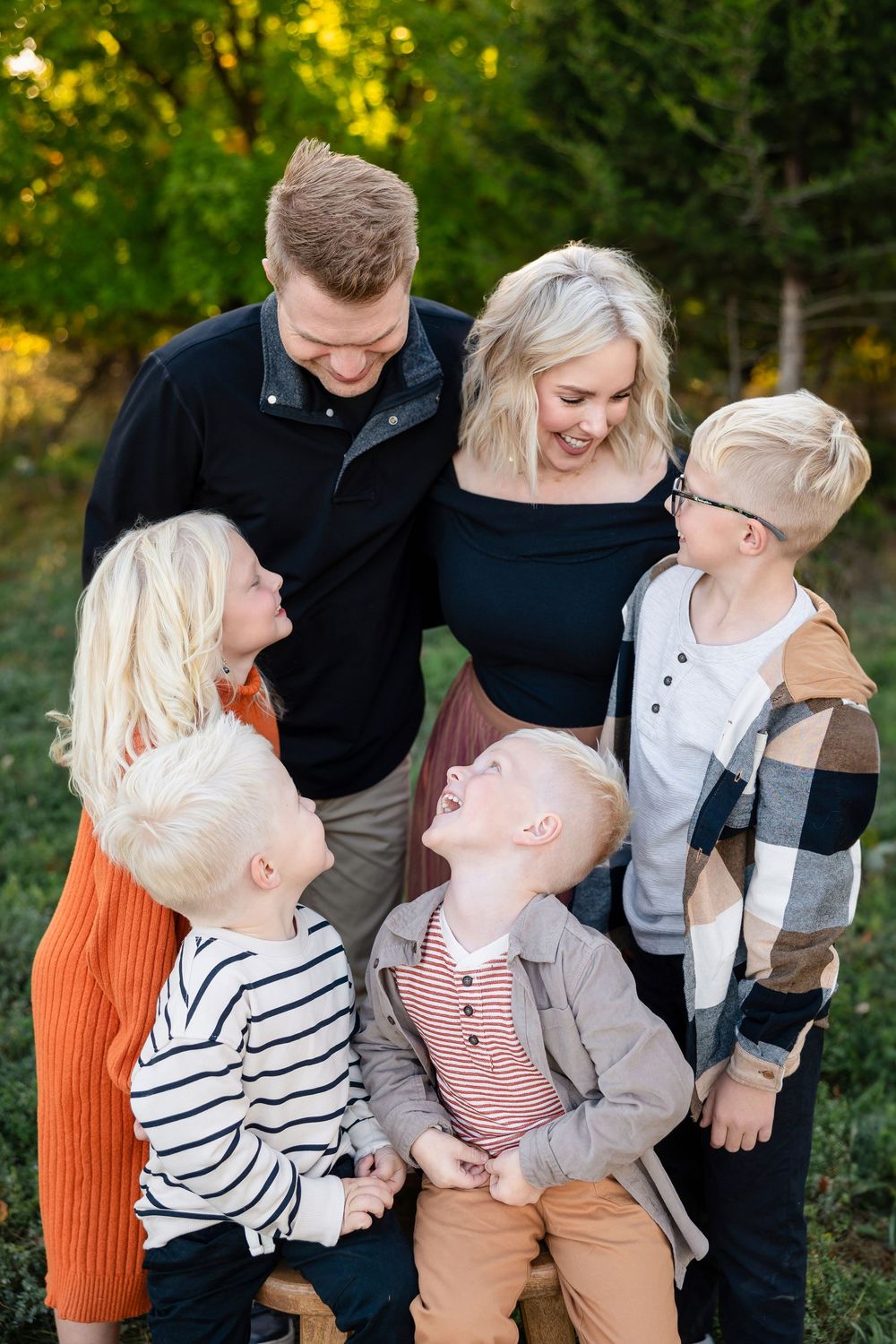 Group wearing coordinated autumn outfits sharing joyful laughter together during outdoor family photo session.
