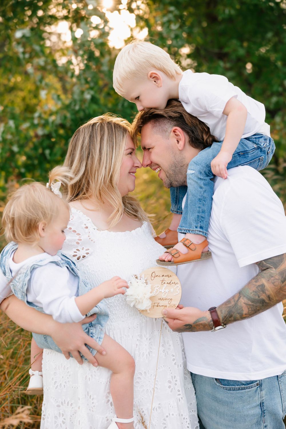 Family sharing intimate moment while holding decorative sign outdoors.