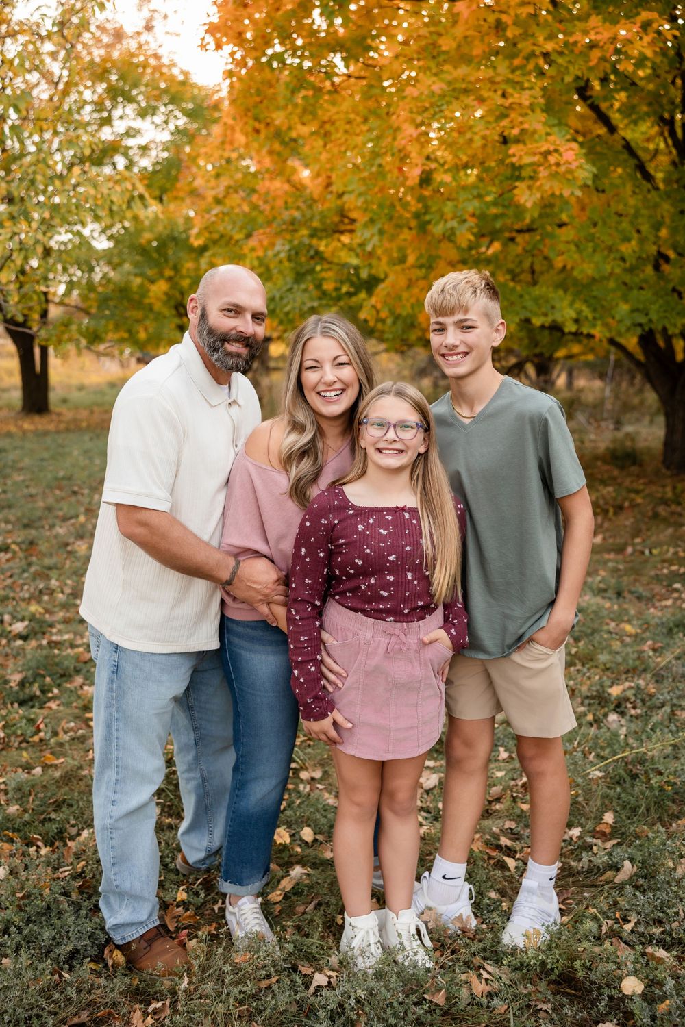 A happy family of four poses together for a portrait among fall foliage and trees.