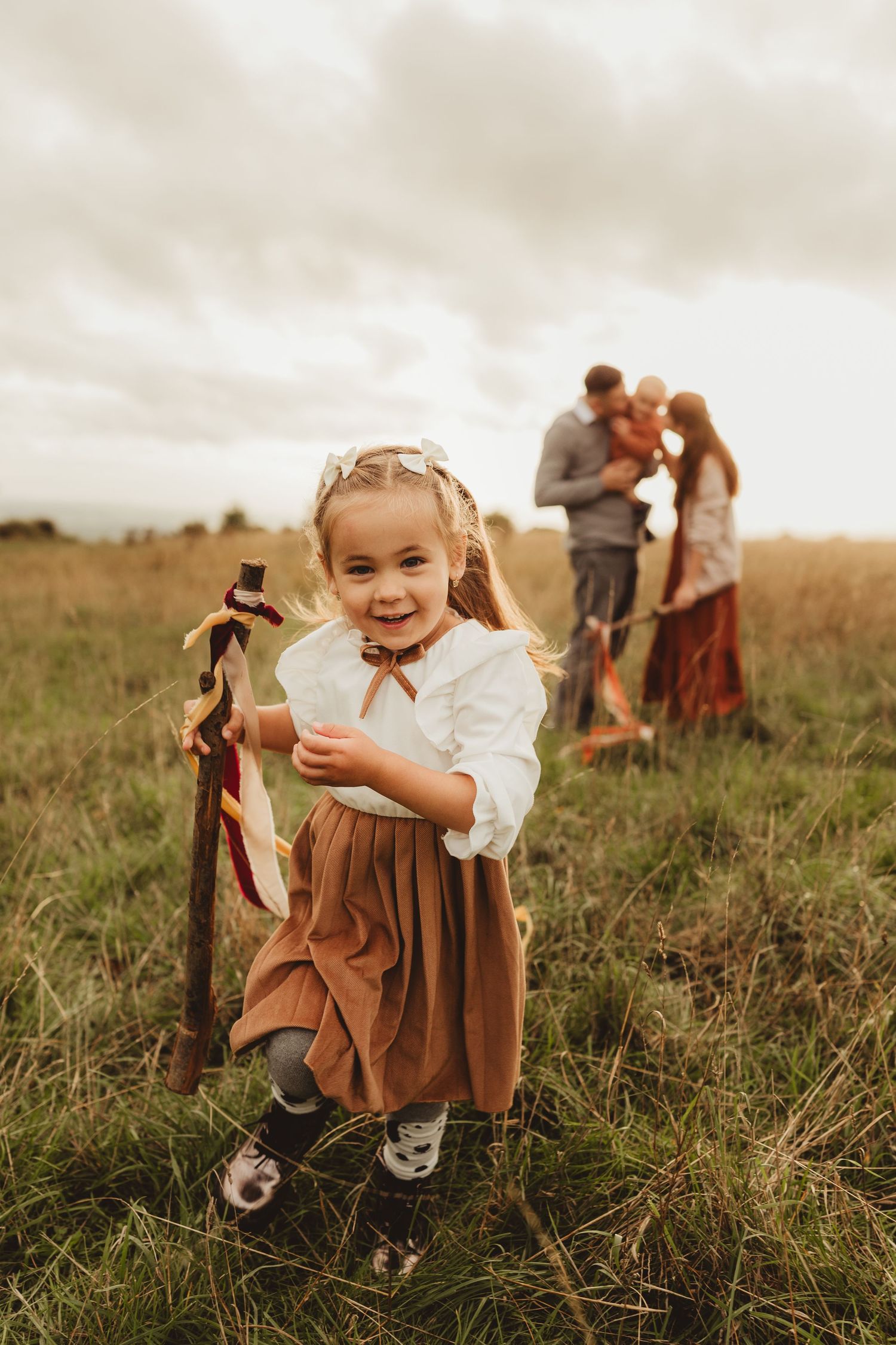 A girl in a flowing coloured lace dress stands in a sunlit field during golden hour.