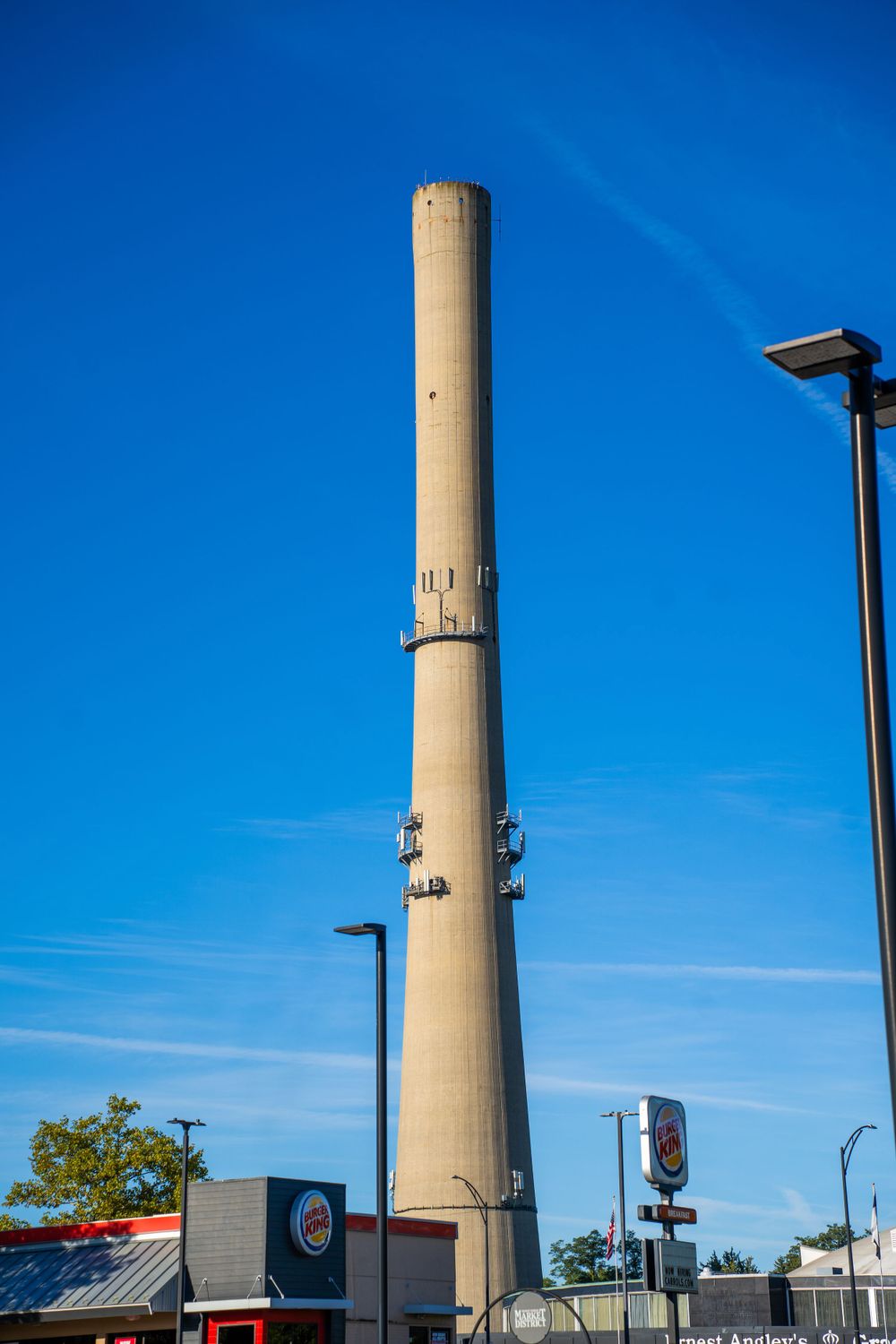 Tall concrete industrial smokestack against a bright blue sky near a Burger King.