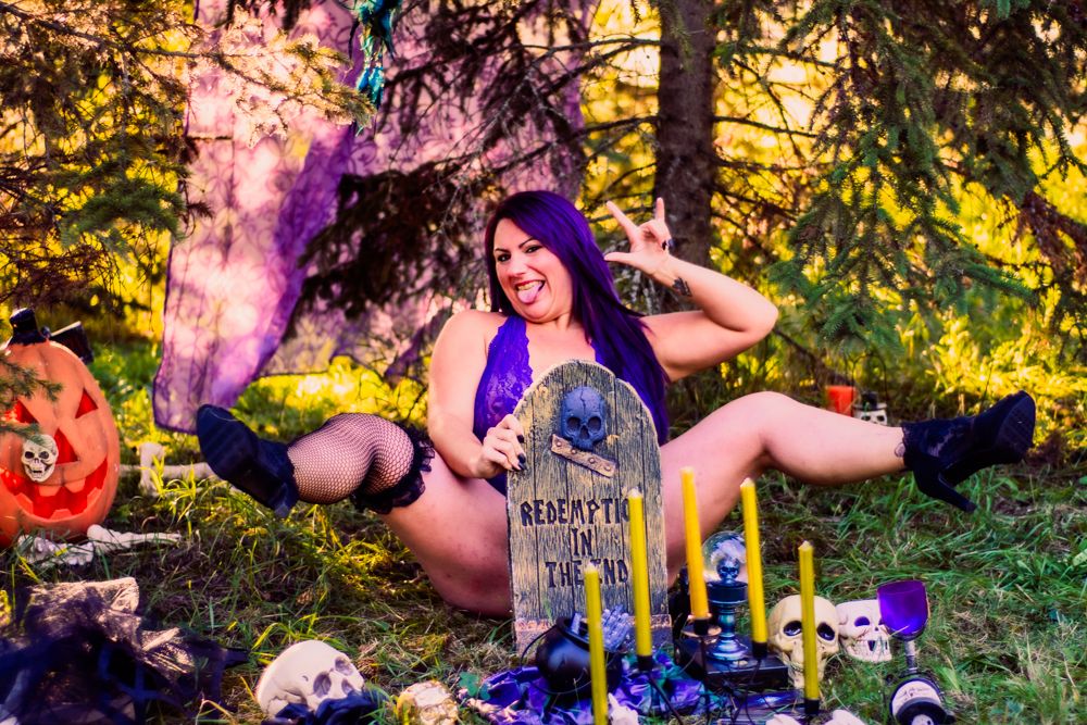 Spooky Halloween scene with purple lighting in forest featuring gravestones, skulls, and dark decorations.