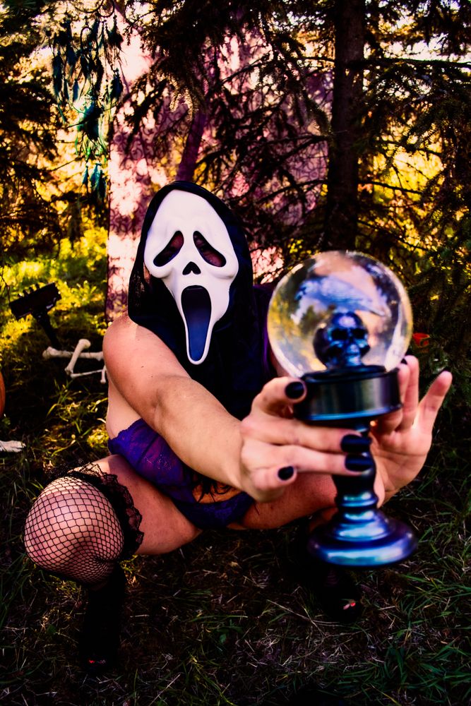 Scream mask wearer holding crystal ball in spooky forest setting.