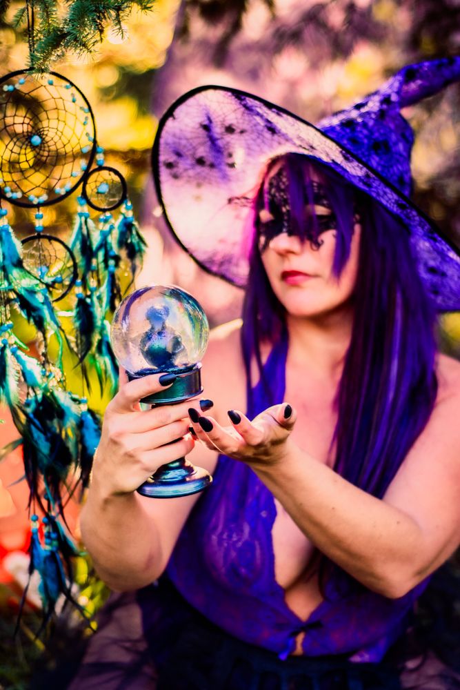 A mystical scene with purple witch hat and crystal ball against yellow bokeh lights and dreamcatcher.