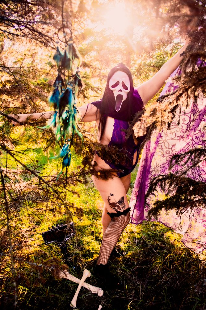 Dramatic Halloween scene with Ghostface mask among crosses and colored lighting in forest.