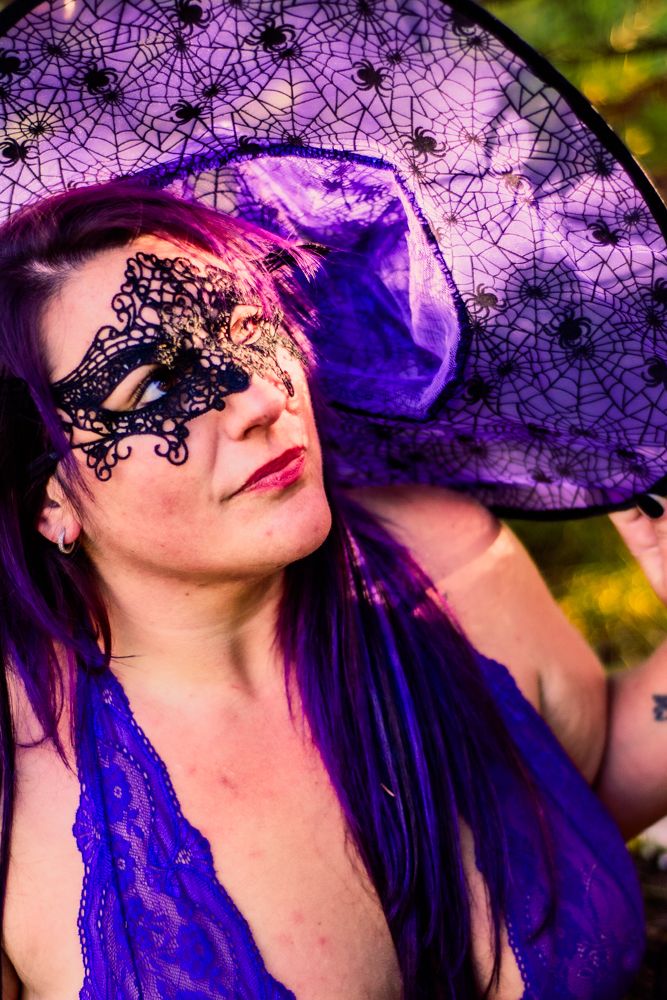 Purple witch hat with spider web pattern and black lace mask against golden sunset.
