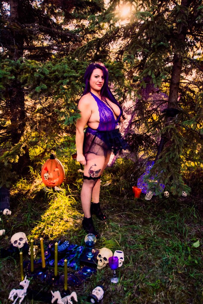 Halloween themed photoshoot with purple accents, pumpkins and skull decorations in forest setting.