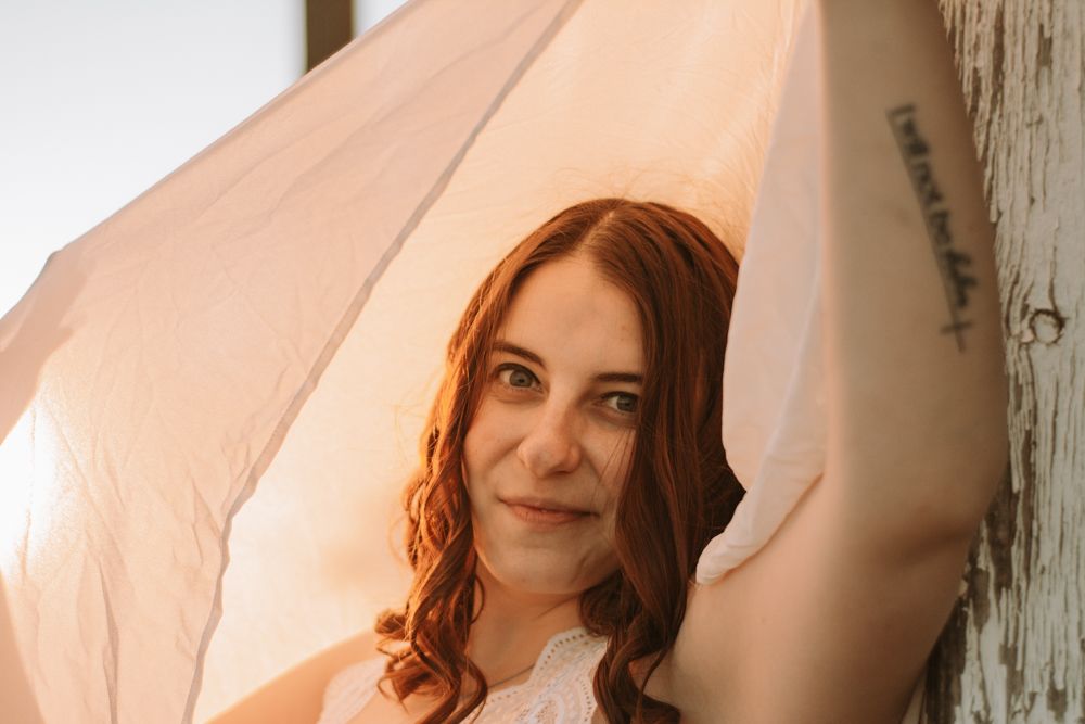 Portrait shot of someone draped in soft white fabric with auburn curls in warm lighting.