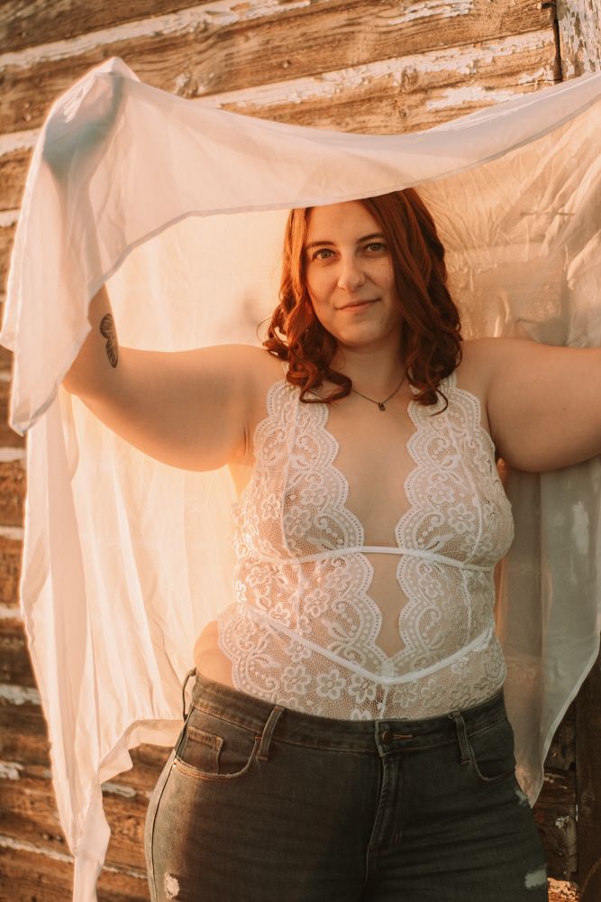 A boudoir portrait featuring white lace lingerie against rustic wooden walls.