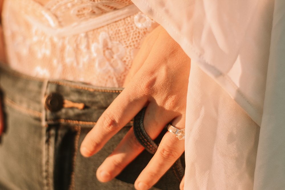 Hand wearing a dark ring visible through sheer white fabric.