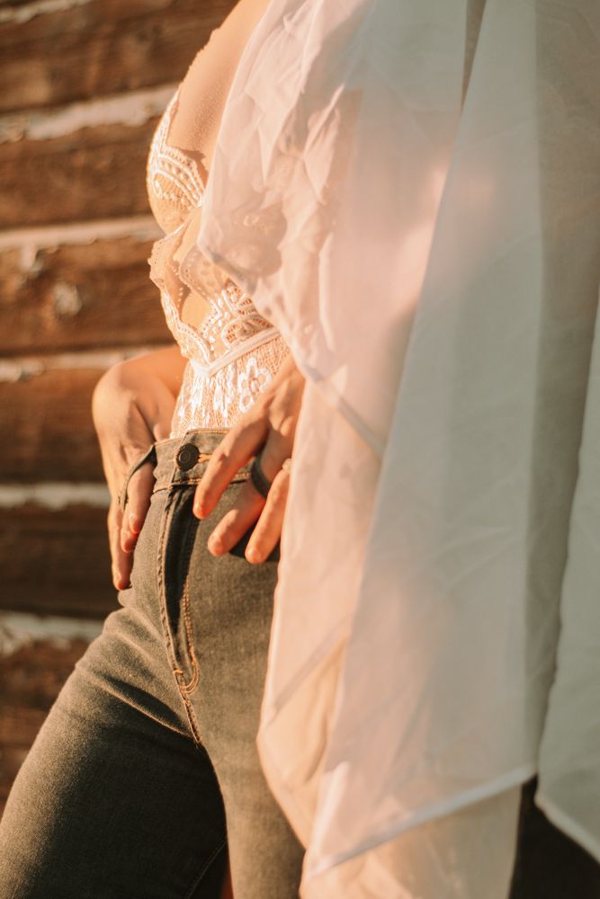 Detail shot of hands resting on denim jeans with lace and flowing white fabric.