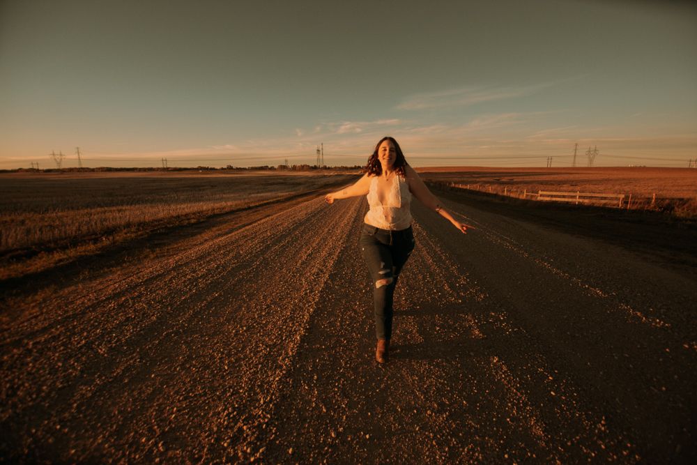 Silhouette of a person running down a country road at sunset with arms outstretched.